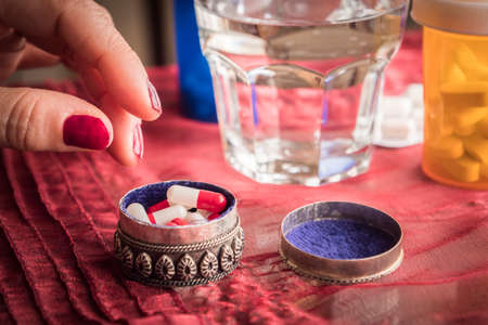 Hand women take capsules red and white in a pillbox metalic old