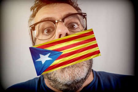 Spanish man with pro-independence flag catalonia covering the mouth, conceptual imageの写真素材