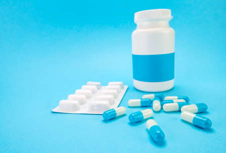Pills spilling from an open bottle on blue background