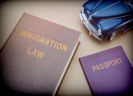 Immigration law book next to a passport and blue miniature vehicle, conceptual image