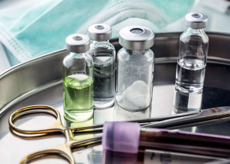 Scissors and vials of blood samples in a tray on a table of a hospital, conceptual image