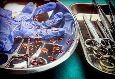 Gloves blue and scissors stained with blood on a tray in an operating theater, conceptual imageの写真素材