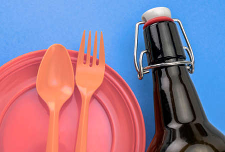Orange dish and plastic cutlery next to a glass bottle, conceptual image