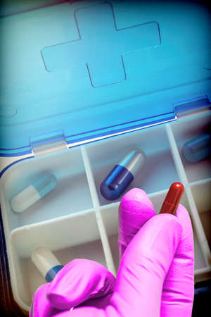 Hand with latex glove supports tablet along with pillbox, conceptual image