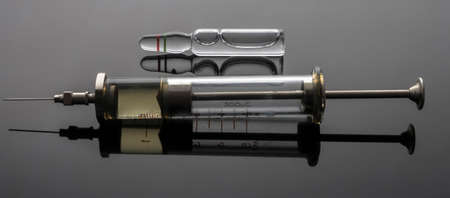 Vintage syringe next to vials with medication, conceptual image, horizontal composition