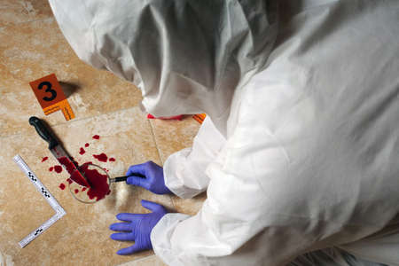 Expert Police examining with magnifying glass a knife with blood at the scene of a crime, conceptual...