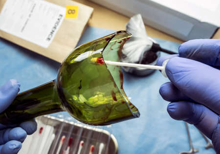 Police expert gets blood sample from a broken glass bottle in Criminalistic Lab, conceptual image