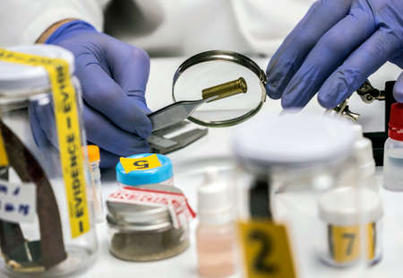 Expert police examines a bullet cap in scientific laboratory with magnifying glassの写真素材