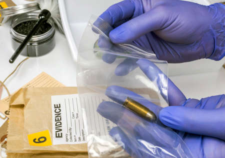 Scientific police picking up bullet in evidence bag, conceptual image