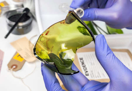 Police expert gets blood sample from a broken glass bottle in Criminalistic Lab, conceptual image
