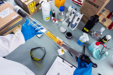 Forensic police remove bloody knife from evidence tube to test suspect's DNA in crime lab, conceptual imageの写真素材