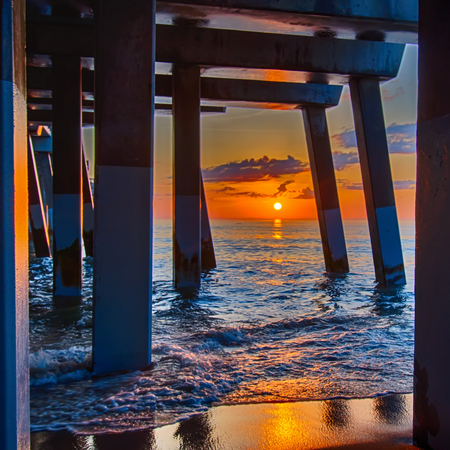 The rising sun peeks through clouds and is reflected in waves by the Nags Head fishing pier on the outer banks of North Carolinaの写真素材