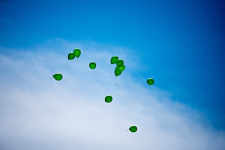green balloons filled with helium flying towards blue sky