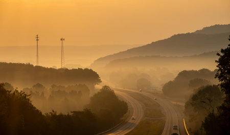 Highway Through Misty Mountain Landscape at Sunrise with Golden Light Fog and Rolling Hills Creating Atmospheric Scenic View