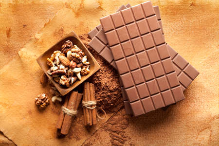 Four chocolate bars, cinnamon sticks, cocoa and mixed nuts in a bowl