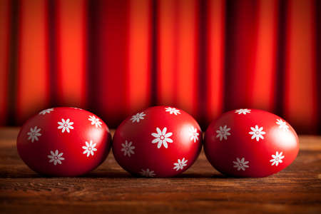 Three red Easter eggs on wooden table and red curtain background