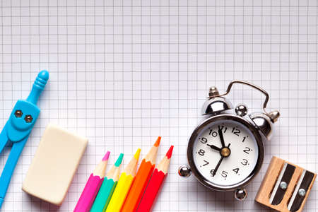 School supplies and alarm clock on notebook  background
