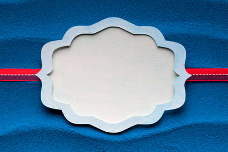Paper label and red ribbon on blue sand backgroundの写真素材