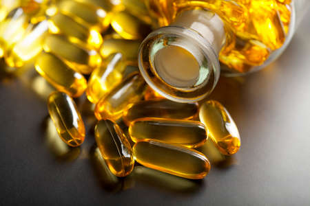 Yellow capsules and glass medical container on black backgroundの写真素材