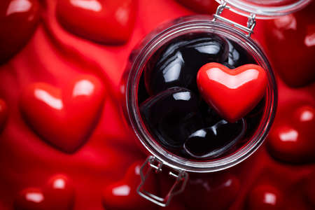 Glass jar full of black hearts and red heart on top and red backgroundの写真素材