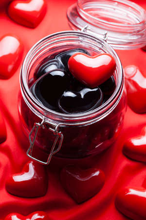 Glass jar full of black hearts and red heart on top and red backgroundの写真素材