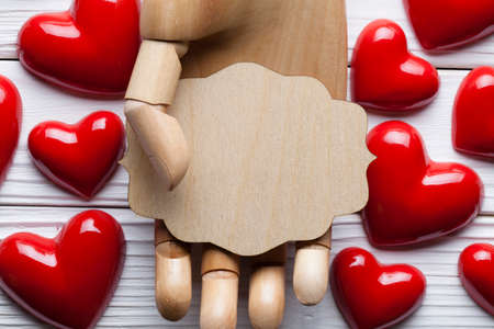 Blank wooden plate in wooden hand and red hearts in backgroundの写真素材