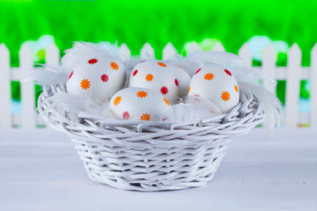 Easter eggs in the basket, wooden fence and green grass on backgroundの写真素材