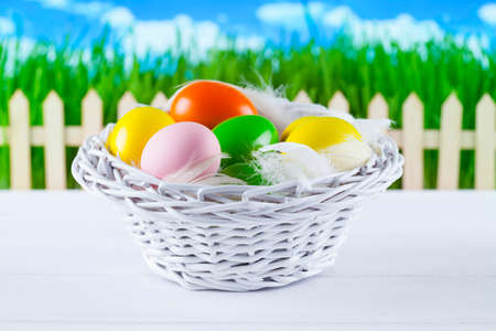 Colored easter eggs in the basket, wooden fence and grass on blue sky backgroundの写真素材