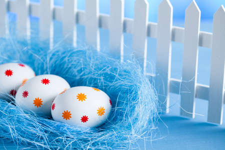 Three easter eggs in the nest and white fence on blue backgroundの写真素材