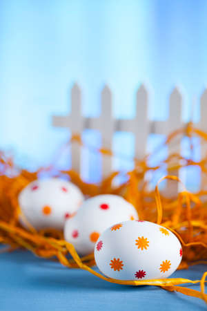 Three easter eggs in the nest and white fence on blue backgroundの写真素材
