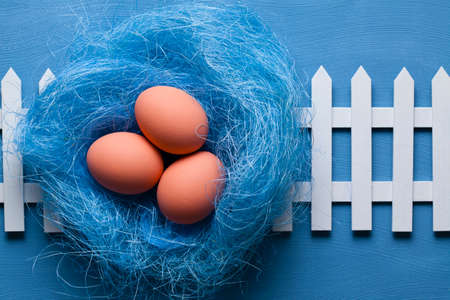 Three easter eggs in the nest and white fence on blue backgroundの写真素材
