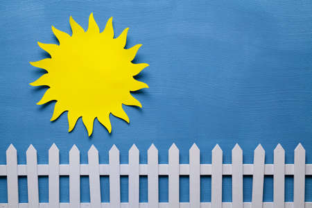 Sun cut out of paper and wooden fence on a blue backgroundの写真素材