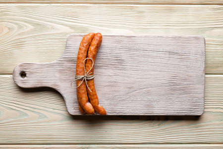 Raw sausage on old damaged cutting board on wooden tableの写真素材