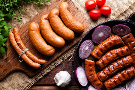 Raw and cooked sausage, pan, herbs and vegetables on wooden tableの写真素材