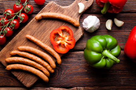 Raw sausage and vegetables on wooden boardの写真素材