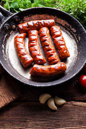 Grilled sausage in a pan and fresh vegetables on wooden tableの写真素材