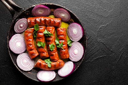 Grilled sausage with onion in a pan on black backgroundの写真素材