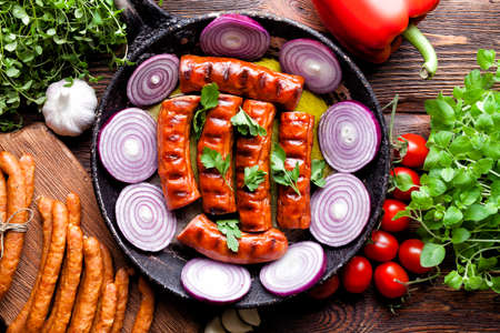 Grilled and raw sausage, fresh herbs and vegetables on wooden tableの写真素材