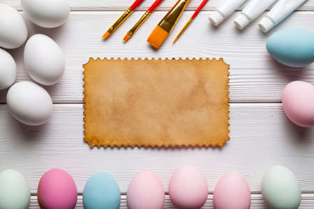 Painting Easter eggs - brushes, paints, eggs and blank paper sheet on white wooden planksの写真素材