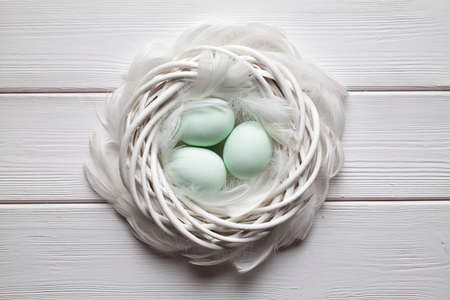 Three easter eggs and feathers in the nest on wooden tableの写真素材