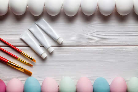 White and painted Easter eggs, brushes and paints on wooden table as a symbol of painting Easter eggsの写真素材