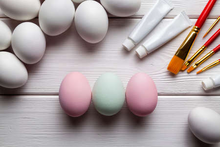 Three painted Easter eggs and many white eggs, brushes and paints on wooden backgroundの写真素材