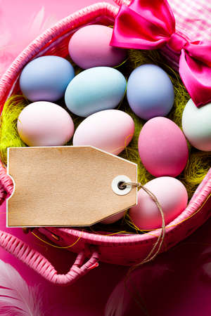 Easter background - blank handmade paper sheet and colored eggs in a basketの写真素材