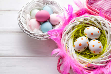 White and colored Easter eggs in basket on white wooden backgroundの写真素材