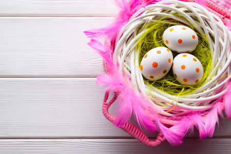 Easter eggs in the nest and pink basket on white wooden tableの写真素材