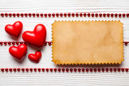 Four red hearts and handmade paper card on white planks の写真素材