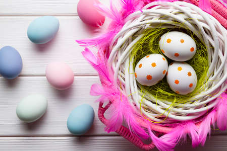 White and colored Easter eggs in basket and on white wooden backgroundの写真素材