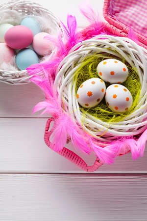 White and colored Easter eggs in basket on white wooden backgroundの写真素材