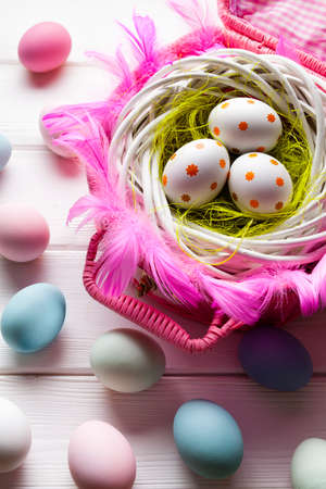 White and colored Easter eggs in basket and on white wooden background