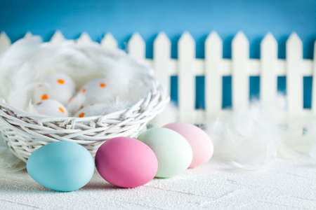 Easter eggs on table and basket, white wooden fence on blue background の写真素材